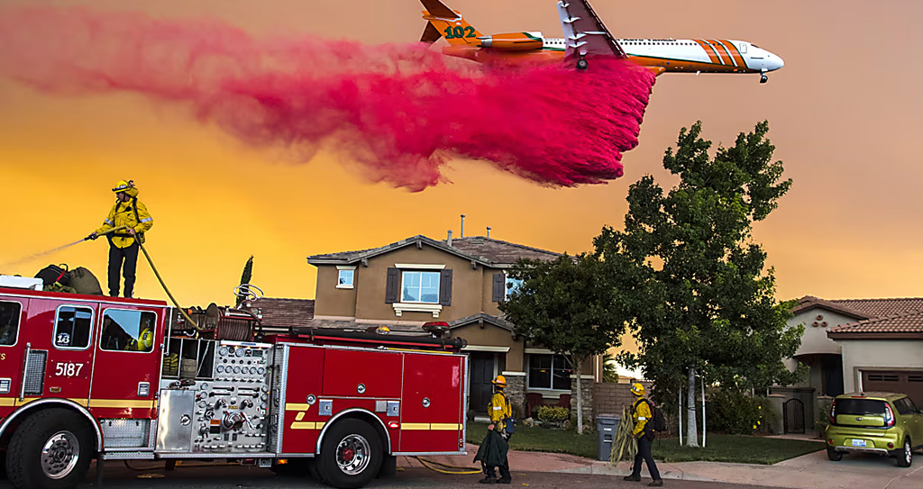 Fire-fighting plane dispensing flame retardant and fire fighting units and engines in front of a home