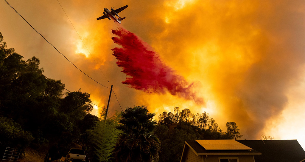 Fire-fighting plane dispensing flame retardant over a neighborhood