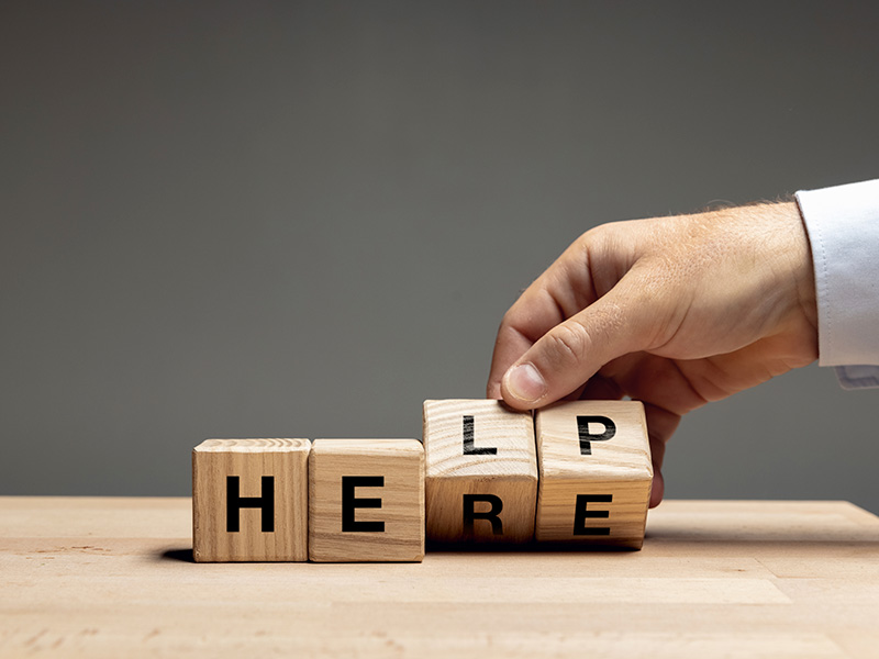 Male hand turning wooden cubes with letters HELP to HERE