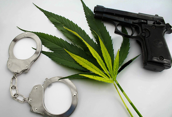 image of a pair of handcuffs set next to a cannabis leaf and a handgun