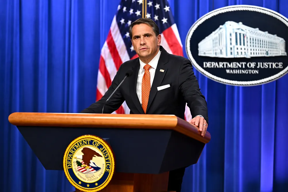 Acting Attorney General Todd Blanche speaks at a Department of Justice podium with U.S. flags and the DOJ seal in the background.